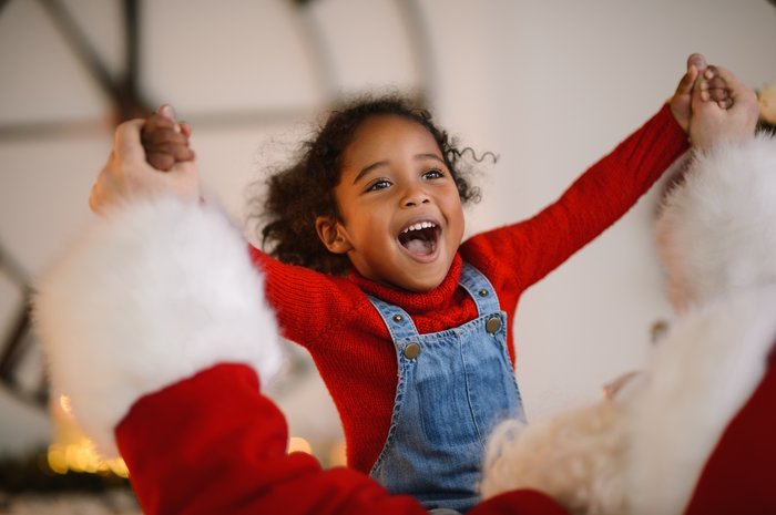 Young girl in a red jumper looking happy sitting with Santa and holding hands
