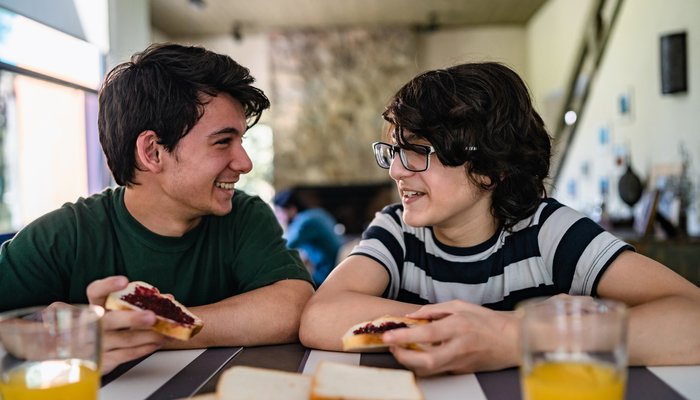 Two brothers smiling at each other as they sit at the table eating toast
