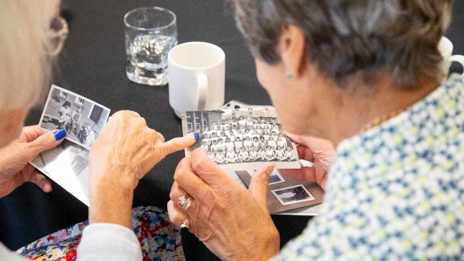 Two older women looking at black and white photograph of old school class