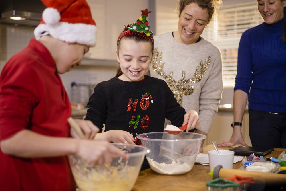 A family wearing Christmas jumpers and novelty Christmas items, baking together in the kitchen