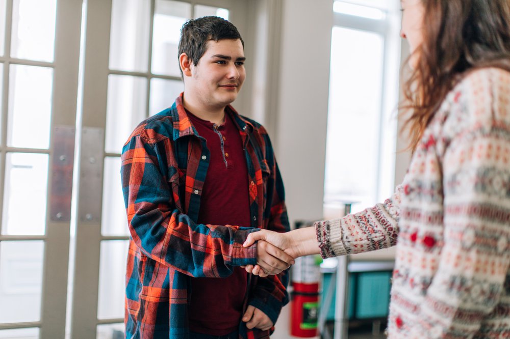 A young female social worker greeting and shaking hands with a a young teenage boy