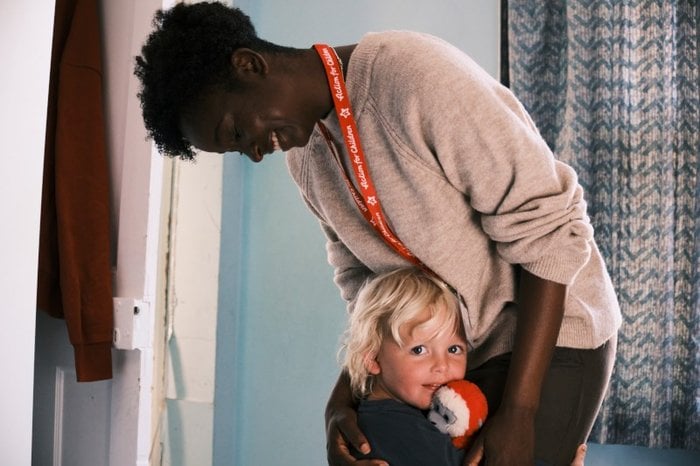 Action For Children worker hugging child who is looking at camera