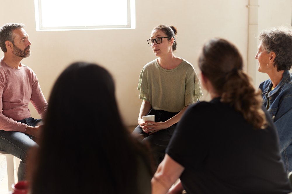 Adult woman talking to others in a support group sat in a circle