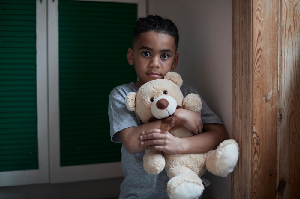 Boy looking into the camera holding a teddy bear