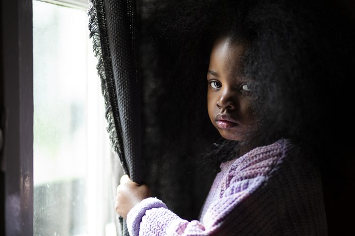 Alice, a sad young girl stands at the window while looking into camera