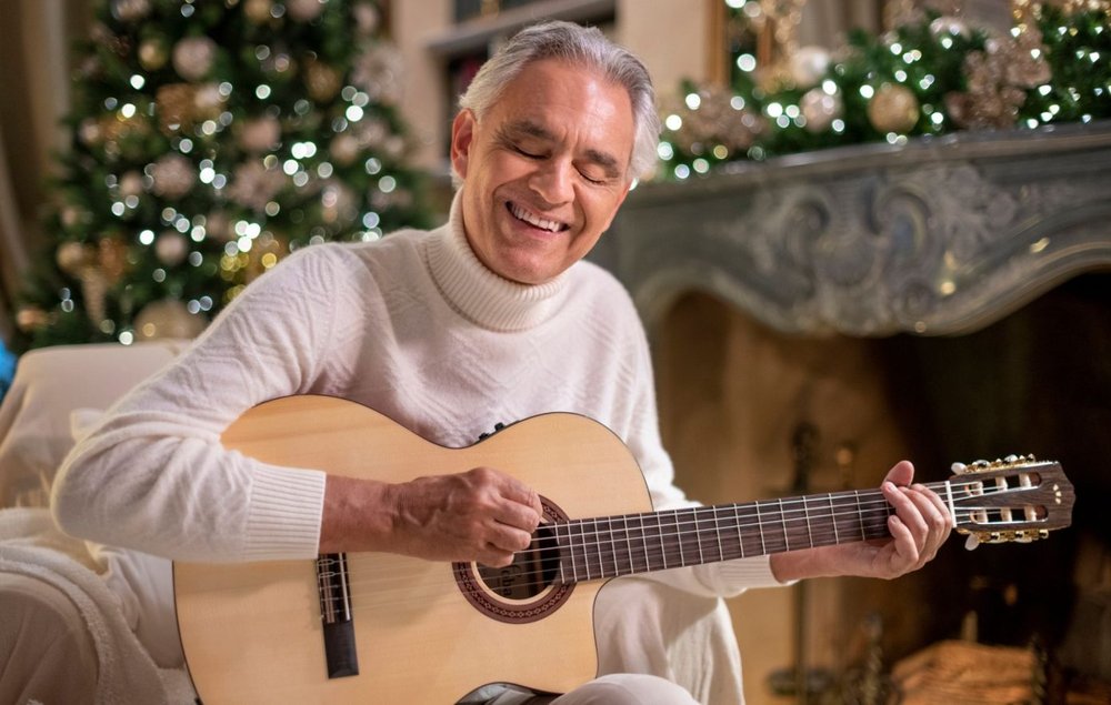 Andrea Bocelli playing guitar against Christmas tree