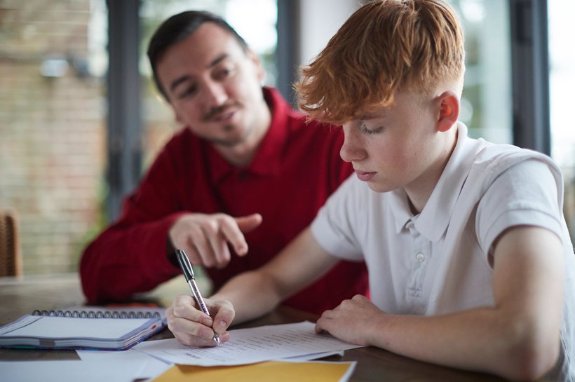 Boy doing work on table and carer helping him