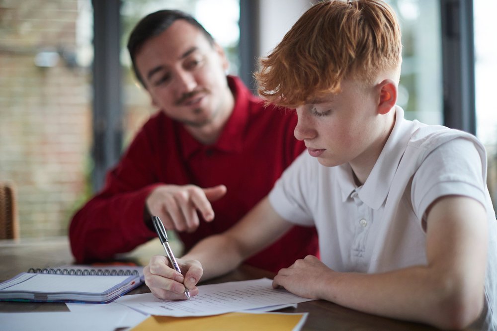 Boy doing work on table and carer helping him