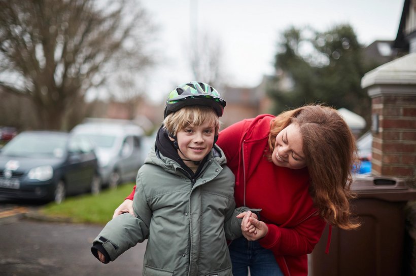 Boy looking into camera with helment held by woman smiling
