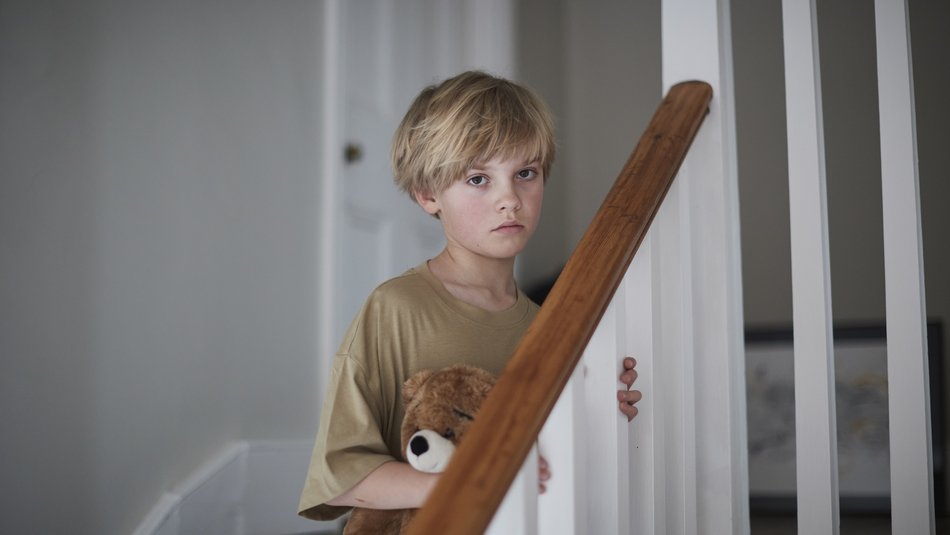 Boy standing on stairs holding teddy looking sad