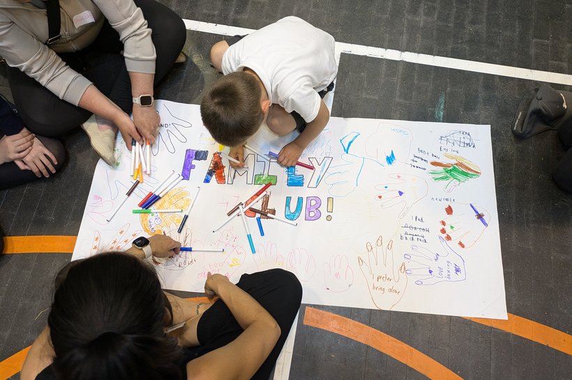 Children drawing the words family club on a big piece of paper on the floor