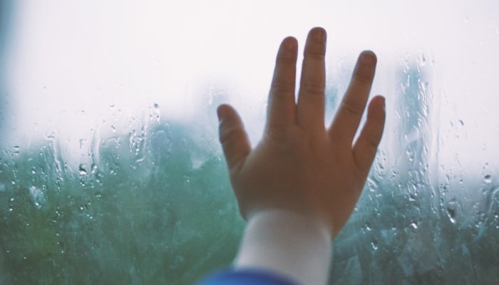 child's hand on rainy window