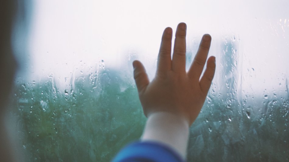 child's hand on rainy window