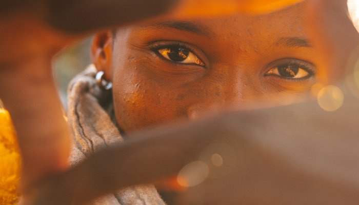 Close up shot of a young girl. You can see her eyes through the camera frame symbol she makes with her hands