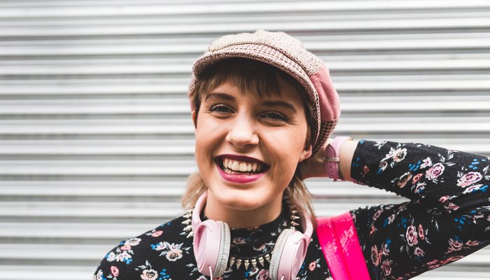Colourfully dressed teenage girl standing against a metal shutter and smiling at the camera