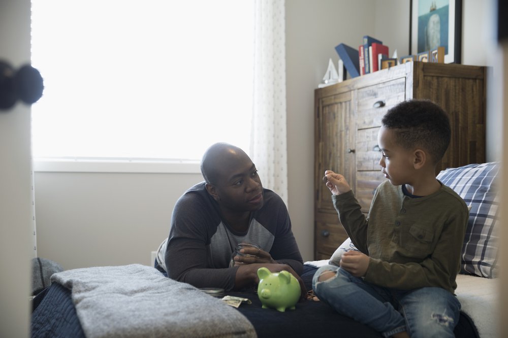 Dad sitting on bed with son and piggy bank