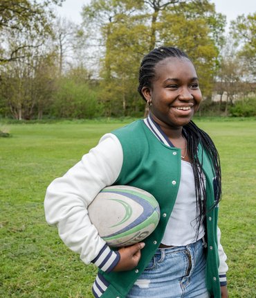 Esther smiling, holding a rugby ball under her arm