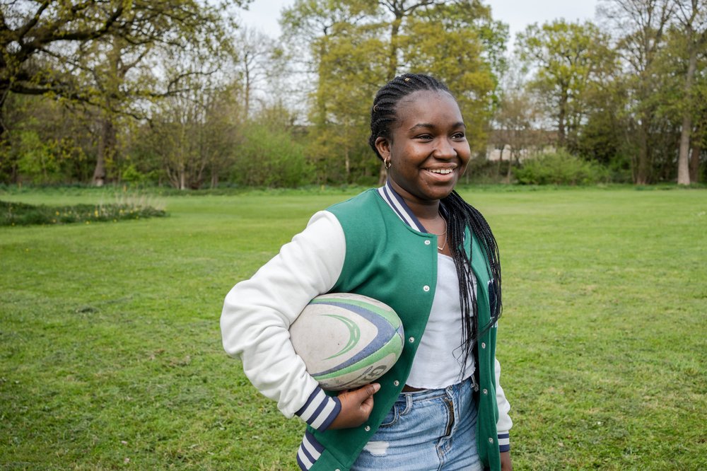 Esther smiling, holding a rugby ball under her arm