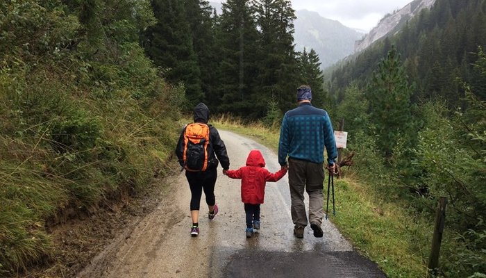 Family with young child hiking on a rainy path through the mountains