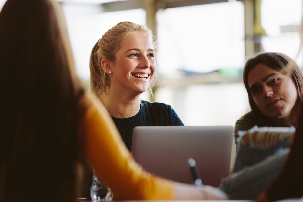Female student sitting at desk amongst classmates and smiling in classroom