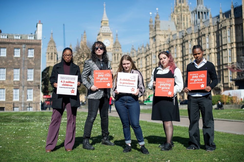 five young campaigners outside parliament holding Paying the Price campaign placquards