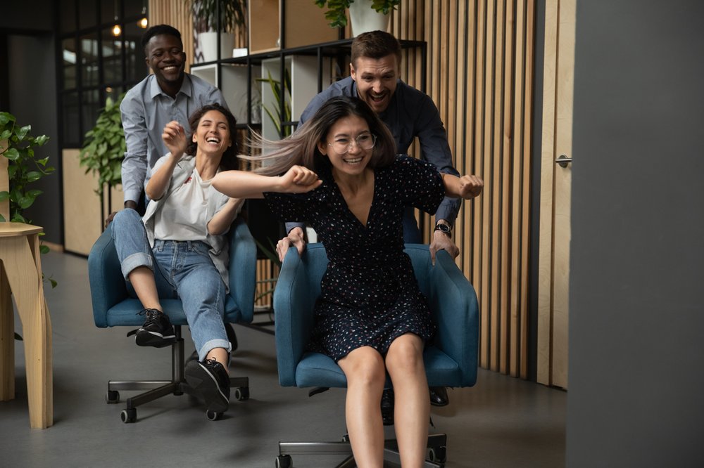 Four young adult staff racing around the office in chairs