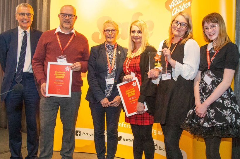 Group of award recipients holding up plaques and certificates during award ceremony