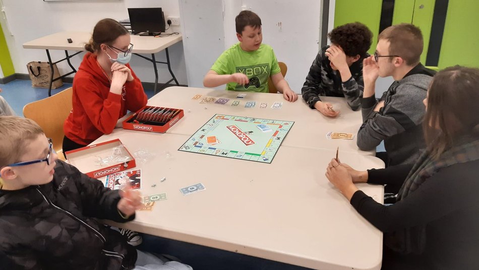 Group of children and young people sitting at a table playing monopoly
