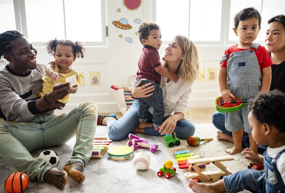 Group of parents and young children at a baby group. They are surrounded by lots of toys on the floor