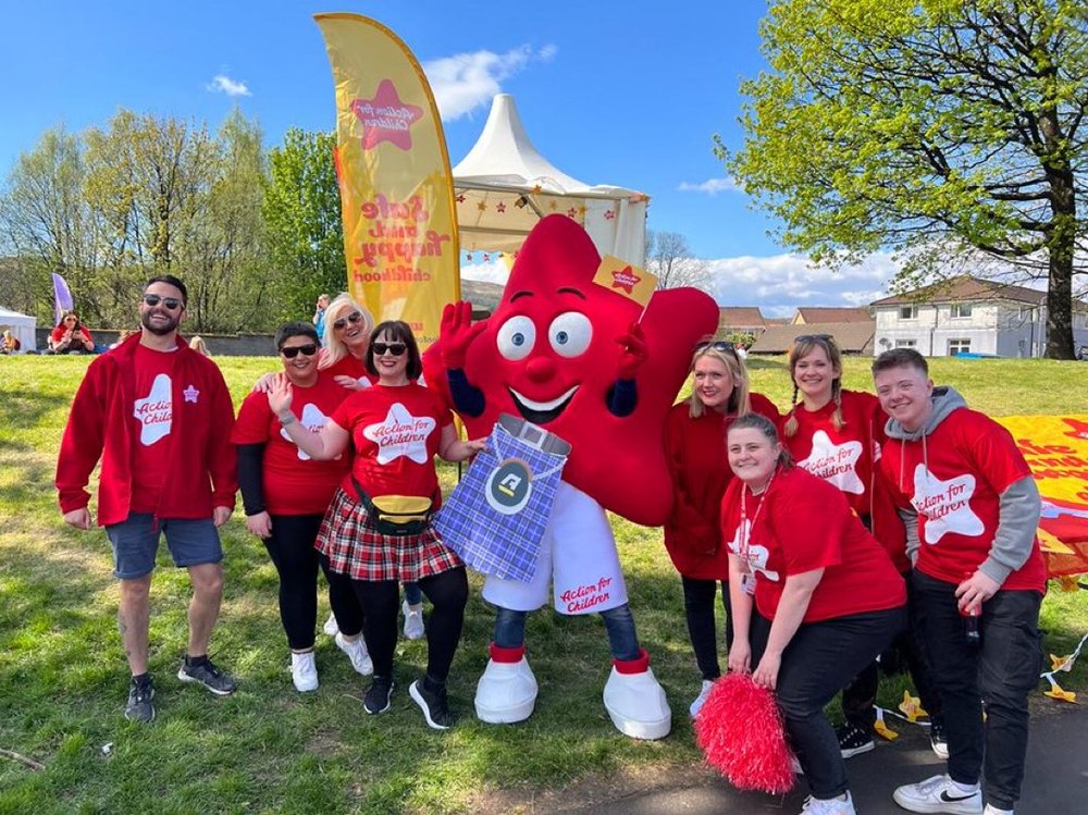 Group of people in Action for Children tshirts smile at camera with Action for Children mascot cosmo