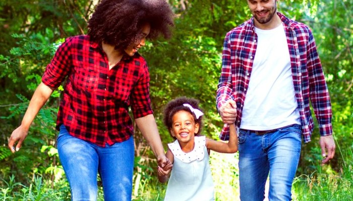 Happy father and mother holding daughters hands and walking through woods