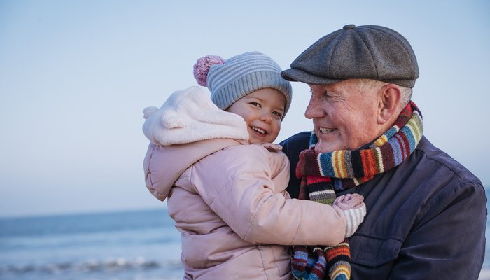 Happy grandfather and toddler hugging on the beach