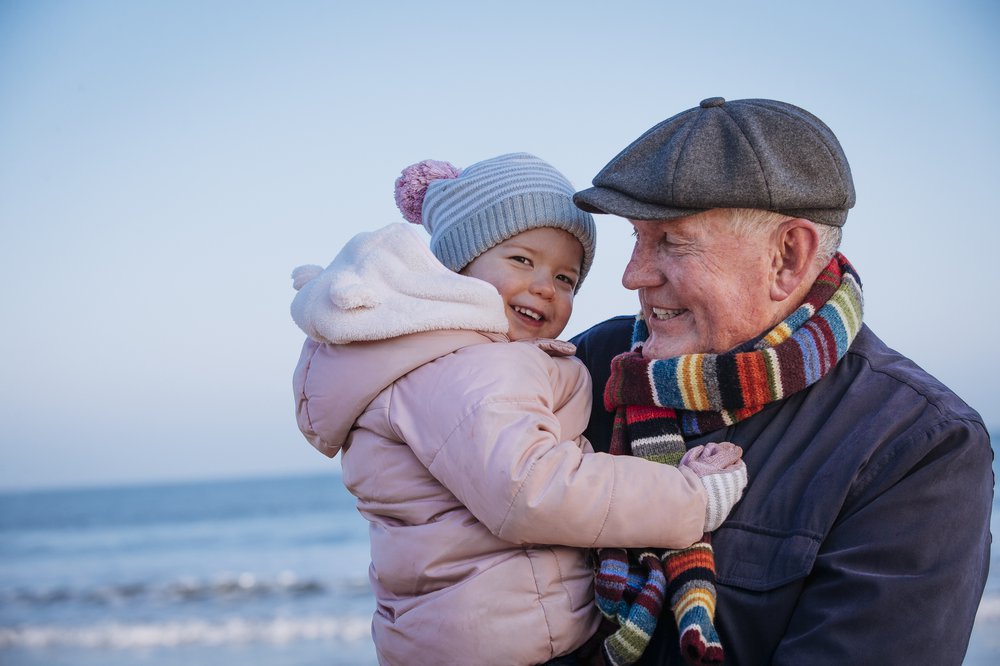 Happy grandfather and toddler hugging on the beach