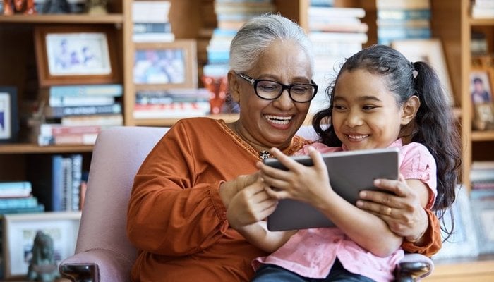 Happy grandmother with smiling daughter on lap reading iPad
