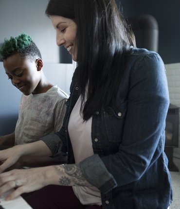 Happy woman and young girl sat playing piano together