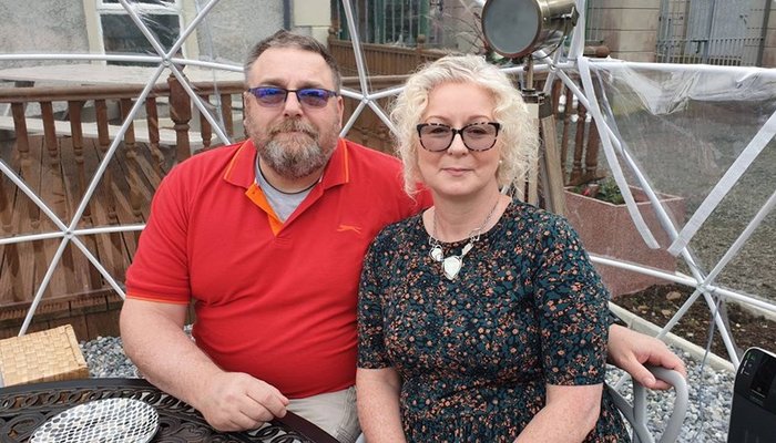 Foster carers John and Geraldine sitting close together at a table outside their home