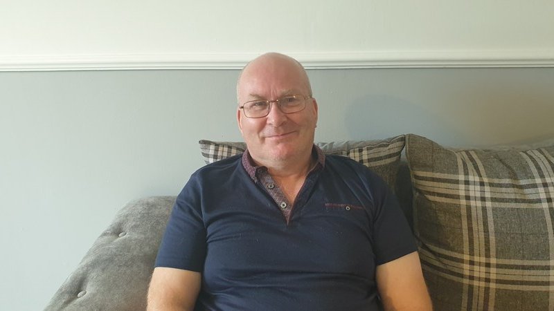 A male foster carer in his home smiling at the camera