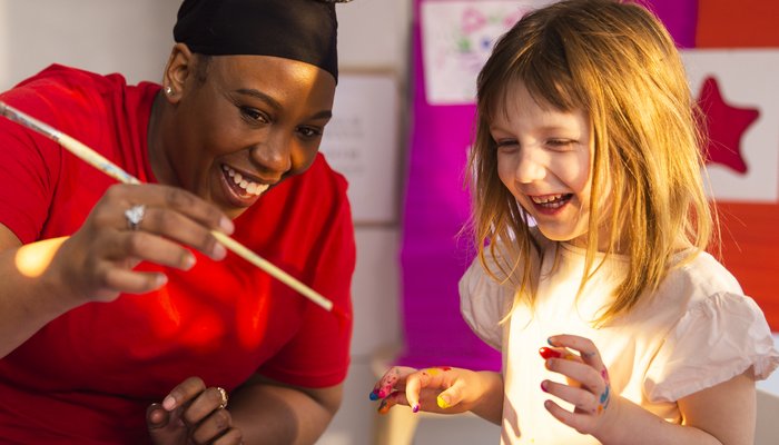 Abby, a young girl, is doing therapy play crafts with her support worker. They are both smiling and laughing.