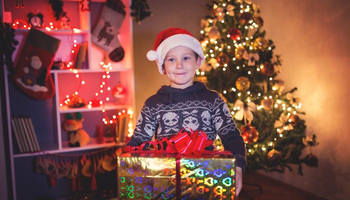 Boy carrying Christmas present in front of Christmas tree