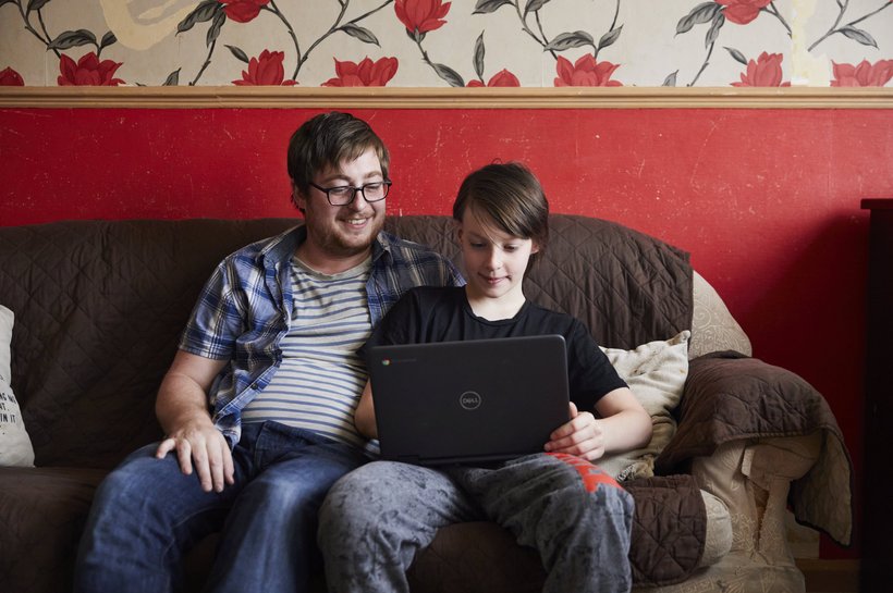 Jacob sitting on a sofa looking at his laptop with his relative sat next to him