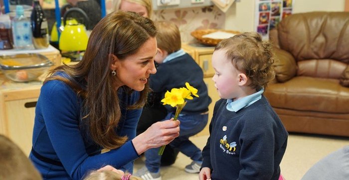 Kate Middleton kneeling down to hand flower to child at Ballymena Sure Start Childrens Centre