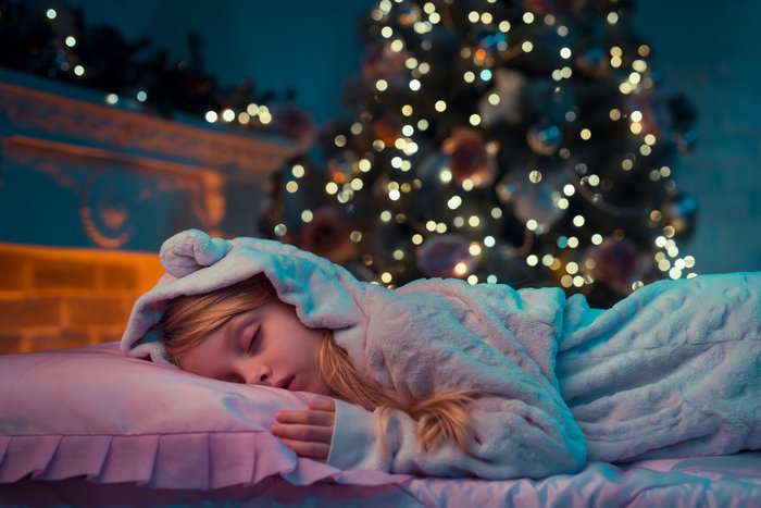 Little girl sleeping in bed with a christms tree in the background