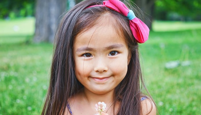 Little girl with long hair standing in field holing flower