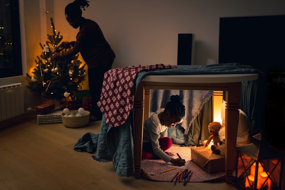 little girl writing down Christmas wish list under the table, in an improvised tent
