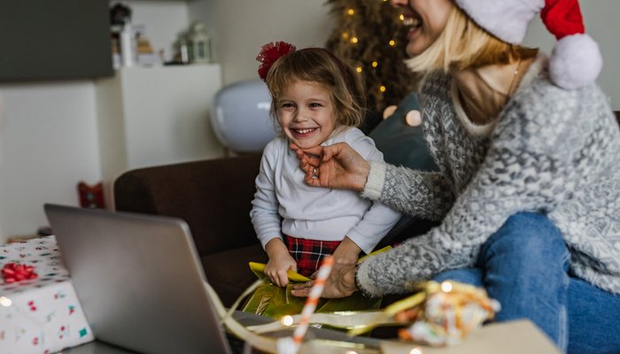 Mother and daughter sat in front of table with laptop and christmas decor on top