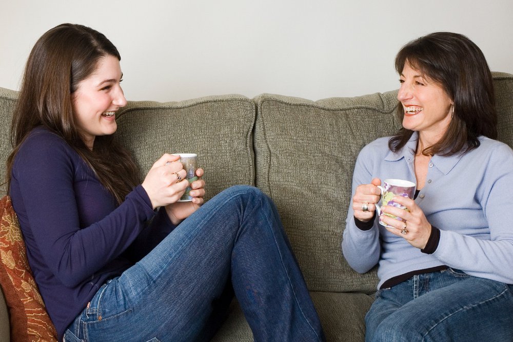 Mother and teenage daughter sitting on sofa and drinking tea together
