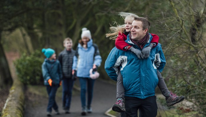 Mother father and their children on a family day out to Bolam Lake in Northumberland. It is cold weather during winter and the father is carrying his young daughter on his back