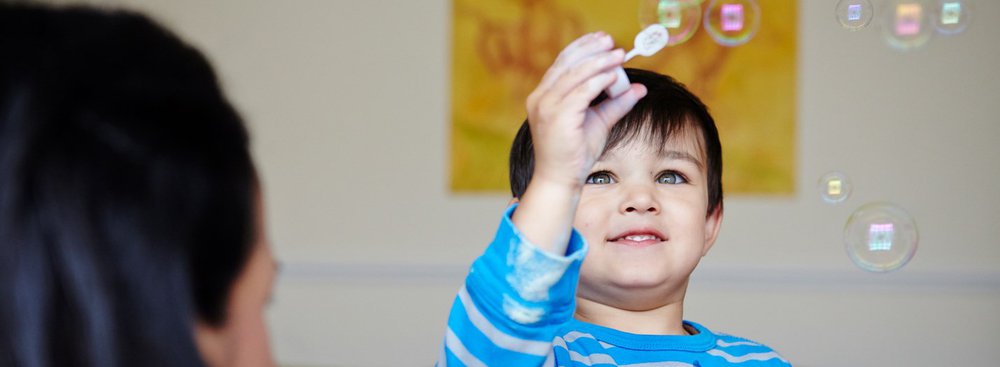 Mother looking at young and happy son blowing bubbles