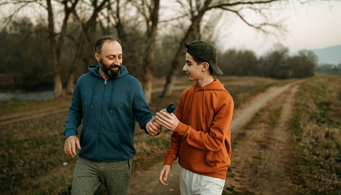 Older man giving a teenage boy a plastic water bottle during the walk in nature