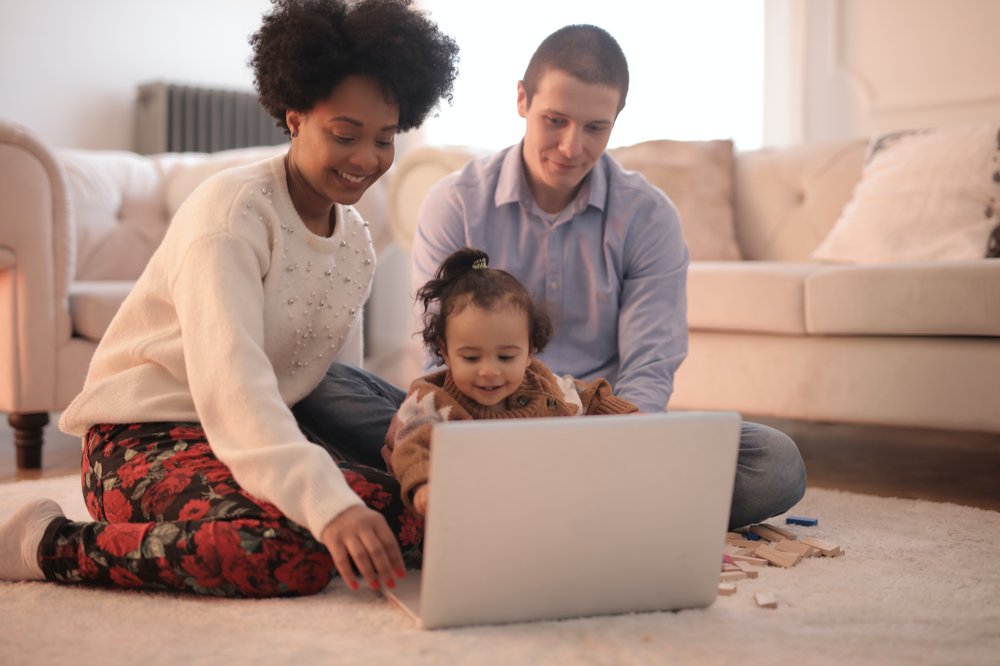 Young couple with baby girl sitting on floor in front of laptop